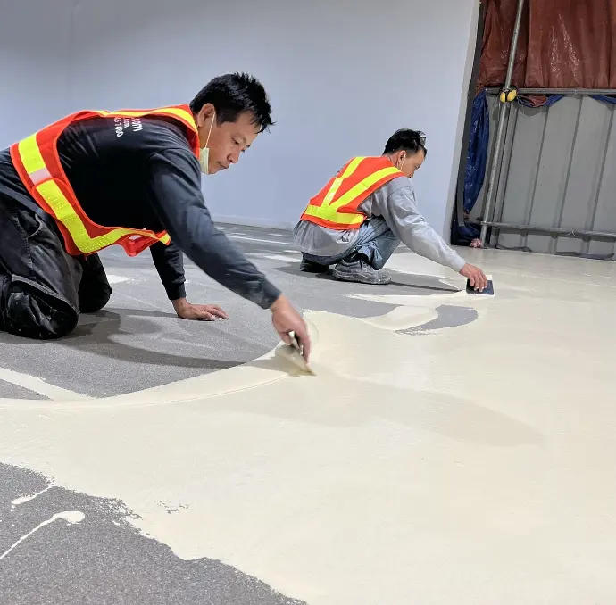 The image depicts two of Carmacoat's applicators spreading epoxy paint on a prepped floor surface