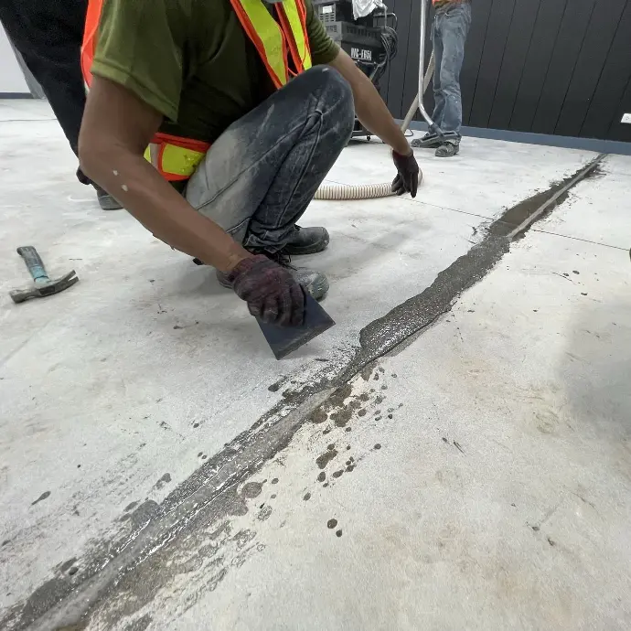 The image depicts a carmacoat employee filling the visible cracks with epoxy grout & mortar using a handheld scraper